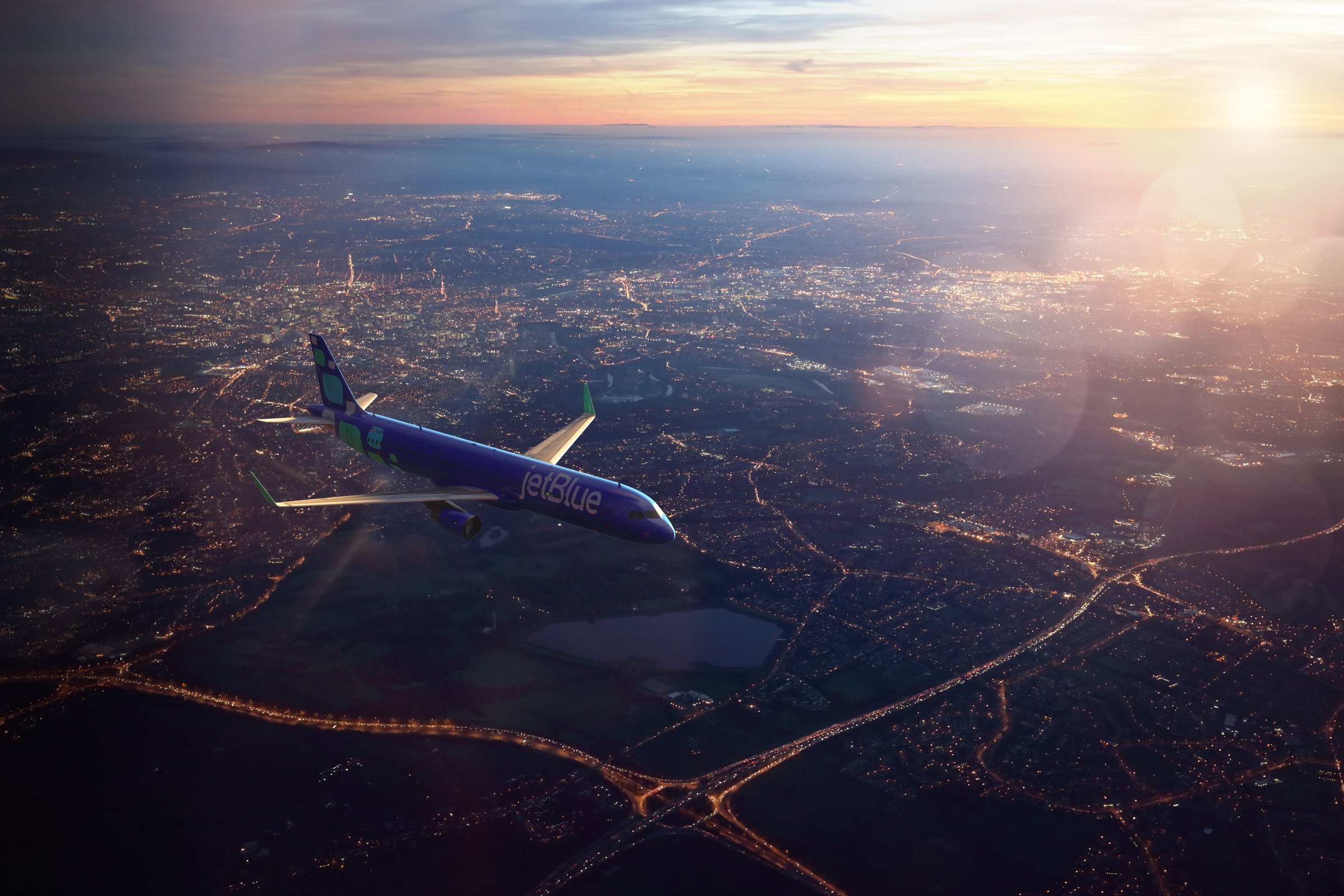 JetBlue A321neo over city lights at sunset